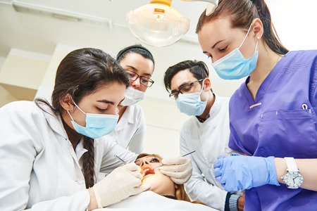 dentistry education. female dentist doctor teacher explaining treatment procedure to iranian asian students group in dental clinic